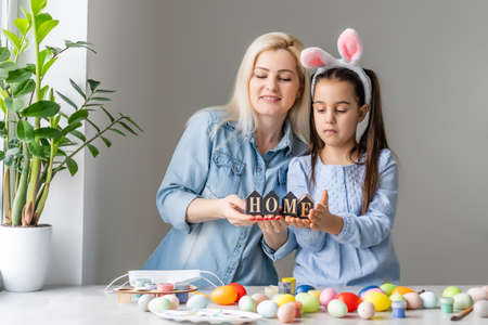 Attractive young woman with little cute girl are preparing for Easter celebration. Mom and daughter wearing bunny ears are spending time together before Easter while painting eggs.の写真素材