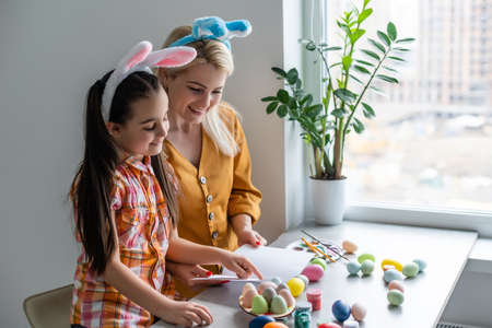 Happy easter. A mother and her daughter painting Easter eggs. Happy family preparing for Easter. Cute little child girl wearing bunny ears on Easter day.の写真素材