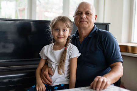 Senior grandfather with small granddaughter indoors sitting at table.の写真素材