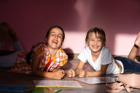 Little girls reading a book in living room. Smart schoolgirls doing their homework after school....