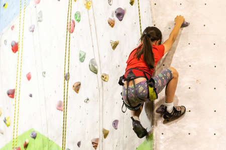 Sporty little girl climbing artificial boulder on practical wall in gymの写真素材