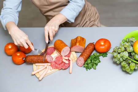 Hand closeup cuts salami with slice pieces at tableの写真素材