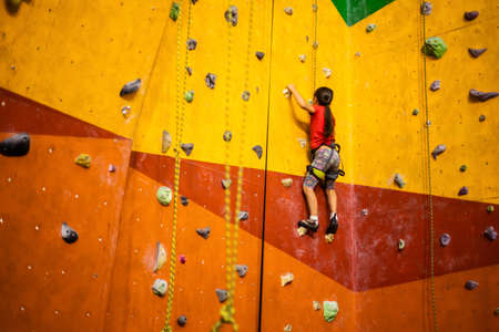 Sporty little girl climbing artificial boulder on practical wall in gymの写真素材