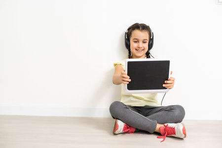 sitting little girl with tablet and headphones