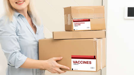a woman in a mask and puffs delivers a box with a vaccineの写真素材