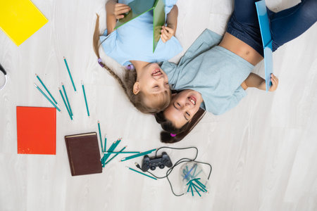 people, children, friends, literature and friendship concept - two happy girls lying on floor and...