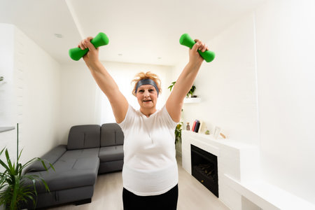 Closeup portrait of active senior woman doing dumbbell exercises at home, smiling.の写真素材
