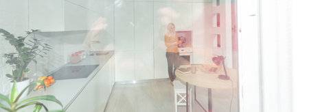 Young woman sitting in kitchen and working on laptop.の写真素材
