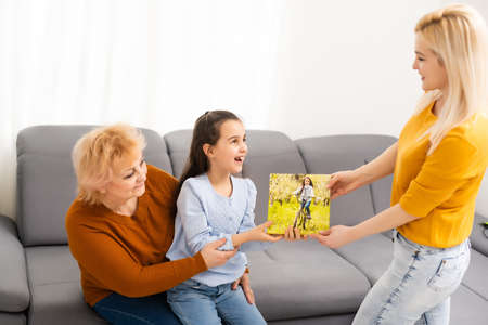 little girl mother and grandmother hold photo canvas in the interiorの写真素材