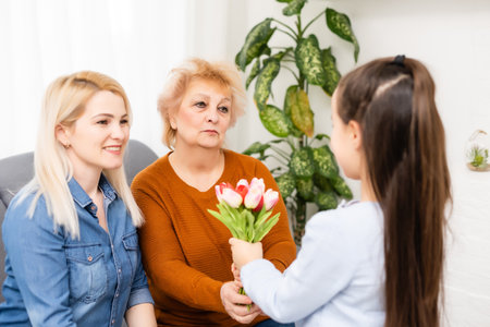 Photo portrait of granddaughter congratulating granny giving tulips bunch sitting near momの写真素材