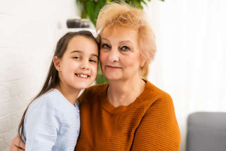 Granny and granddaughter are using a laptop and smiling while sitting on sofa at homeの写真素材
