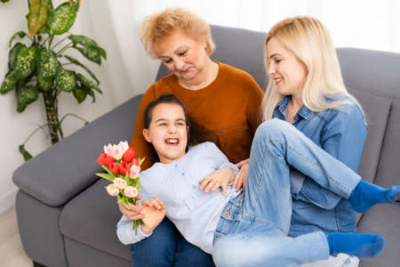 Photo portrait of granddaughter congratulating granny giving tulips bunch sitting near momの写真素材