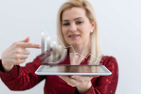 Businesswoman holding digital graphs and charts in her hands at office closeup. Successful business profit growth conceptの写真素材