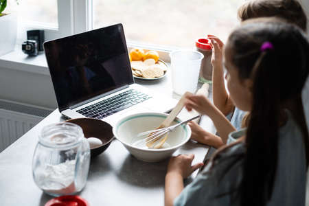 Two little girls in the kitchen prepare food, a dessert for the family. As they learn to cook they start playing with flour and smiling each other. Concept of: cooking classes, family, education.の写真素材