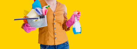 Photo of housewife in gloves holding cleanser bottles over yellow backgroundの写真素材