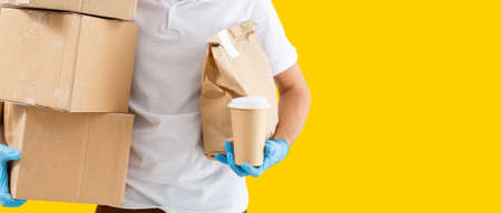 Portrait of delivery man in uniform holding parcel box isolated over yellow backgroundの写真素材