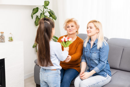 A little girl gives a bouquet of tulips to her mom and grandmother. They celebrate Mothers Day. They...