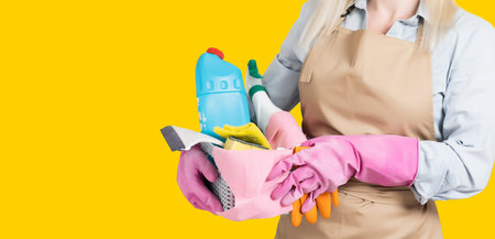 Photo of housewife in gloves holding cleanser bottles over yellow background