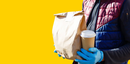 delivery man carrying paper bag with food products isolated over yellow backgroundの写真素材