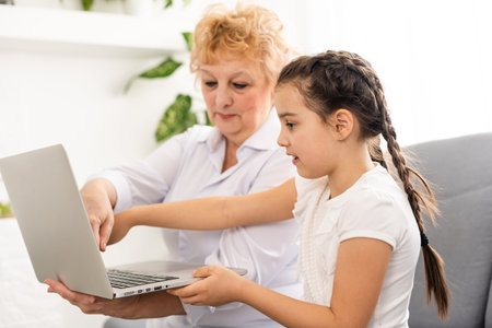 Teen girl distance learning virtual distance online class on video call virtual lesson with grandmother, studying at home using laptop computer. grandParent or tutor helping child daughter with remote education.の写真素材