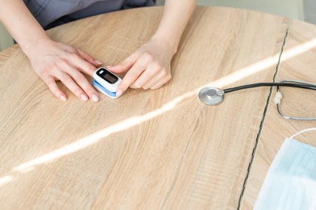 Pulse Oxymeter on a woman finger hand on a wooden table. Top view.