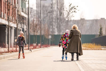 A happy family in roller skates, grandma teaches two granddaughters to roller-skateの写真素材
