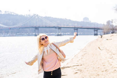 young woman raising arms up towards blue sky and river.の写真素材