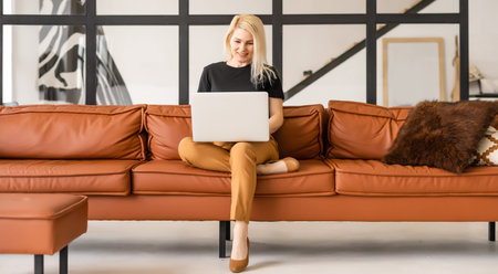 Happy casual beautiful woman working on a laptop sitting in the house.の写真素材