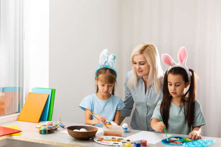Young mother and her two little daughters painting colorful Easter eggs at homeの写真素材