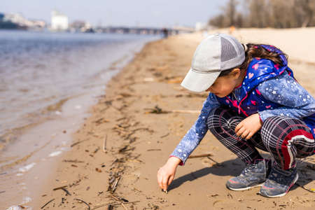 little girl draws on the sand by the riverの写真素材