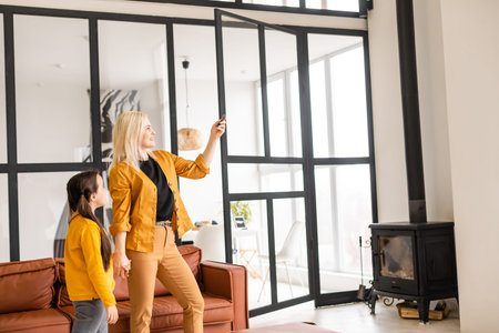 Smiling mom and daughter relaxing, operating air conditioner with remote controller, rest at home, enjoying fresh airの写真素材