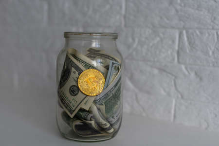 Saving money coin in jar. Symbol of investing, keeping money concept. Collecting cash banknotes in glass tin as moneybox. American dollars close-up with increasing columns of gold coins on tableの写真素材
