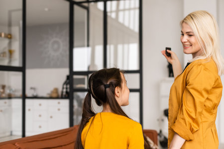 Smiling mom and daughter relaxing, operating air conditioner with remote controller, rest at home,...