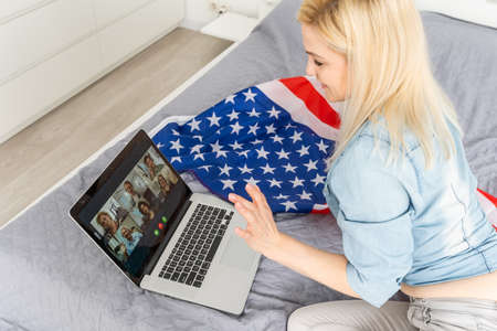Young woman with USA flag using a laptop computer, independence day onlineの写真素材
