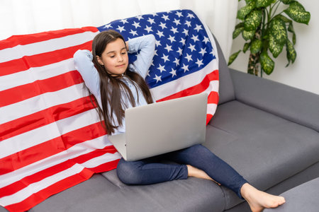 Back to online school education. Difficult to speak English. Kid doing homework on computer. Student studying on laptop over American flag. Tutor teach distantly.の写真素材