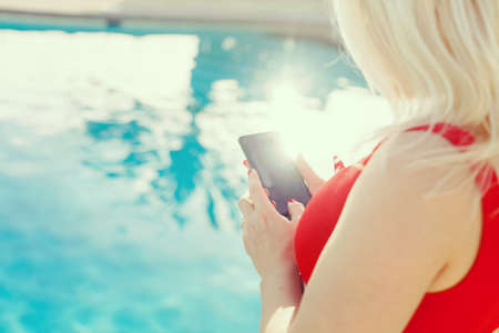 Woman hand using smartphone near swiming poolの写真素材