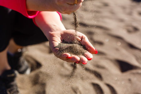 hand pours sand by the sea and rocks. symbol for time running out and time management. nails with manicure.の写真素材