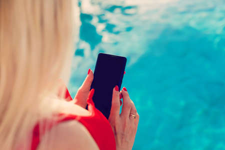 Woman hand using smartphone near swiming poolの写真素材
