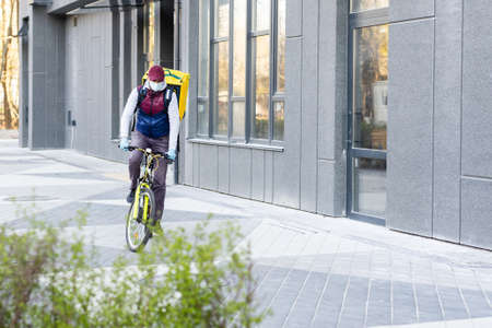 Delivery Man standing with yellow thermo backpack for food delivery near the entrance home with empty space to copy pasteの写真素材