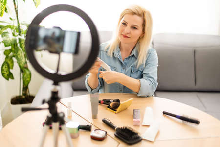 Portrait of beautiful young woman fashion vlogger or blogger reviewing recording video beauty products to share on social media. Cosmetic concept. Making vlog doing a make up tutorial.の写真素材