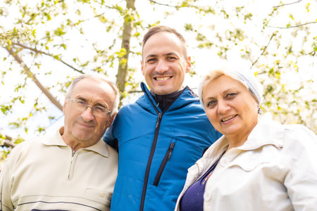 Adult son with his elderly parents outdoors in a natural setting.
