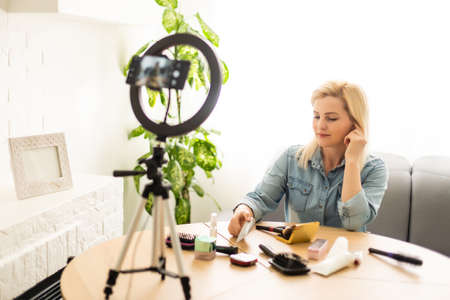 Portrait of beautiful young woman fashion vlogger or blogger reviewing recording video beauty products to share on social media. Cosmetic concept. Making vlog doing a make up tutorial.の写真素材