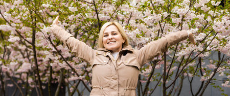 Beautiful woman enjoying sunny spring day in park during cherry blossom season