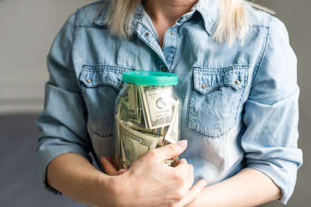 woman holding a transparent jar full of american dollars. Shopping conceptの写真素材