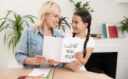 Happy mother hugging her adorable little daughter and holding greeting card for Mothers Day.