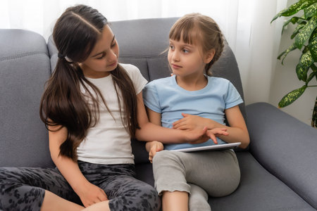 Closeup portrait of two smiling girls lying on couch and using tablet