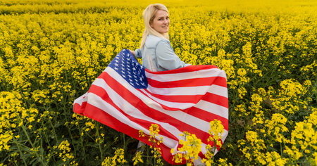 Adult woman holding American flag with pole, stars and stripe in a yellow rapeseed field. USA flag...