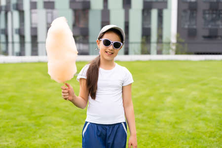 Adorable and pretty curly little girl eating sweet cotton candy. Happy child, kid eating candy-floss with emotions in the park at summer or spring.の写真素材