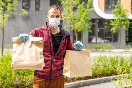 Postal delivery courier man wearing protective face mask in front of cargo van delivering package holding box due to pandemicの写真素材