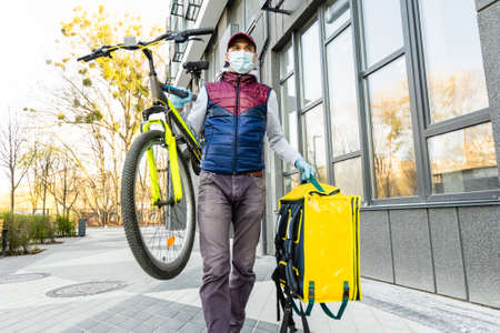 Delivery Man standing with yellow thermo backpack for food delivery near the entrance home with empty space to copy pasteの写真素材